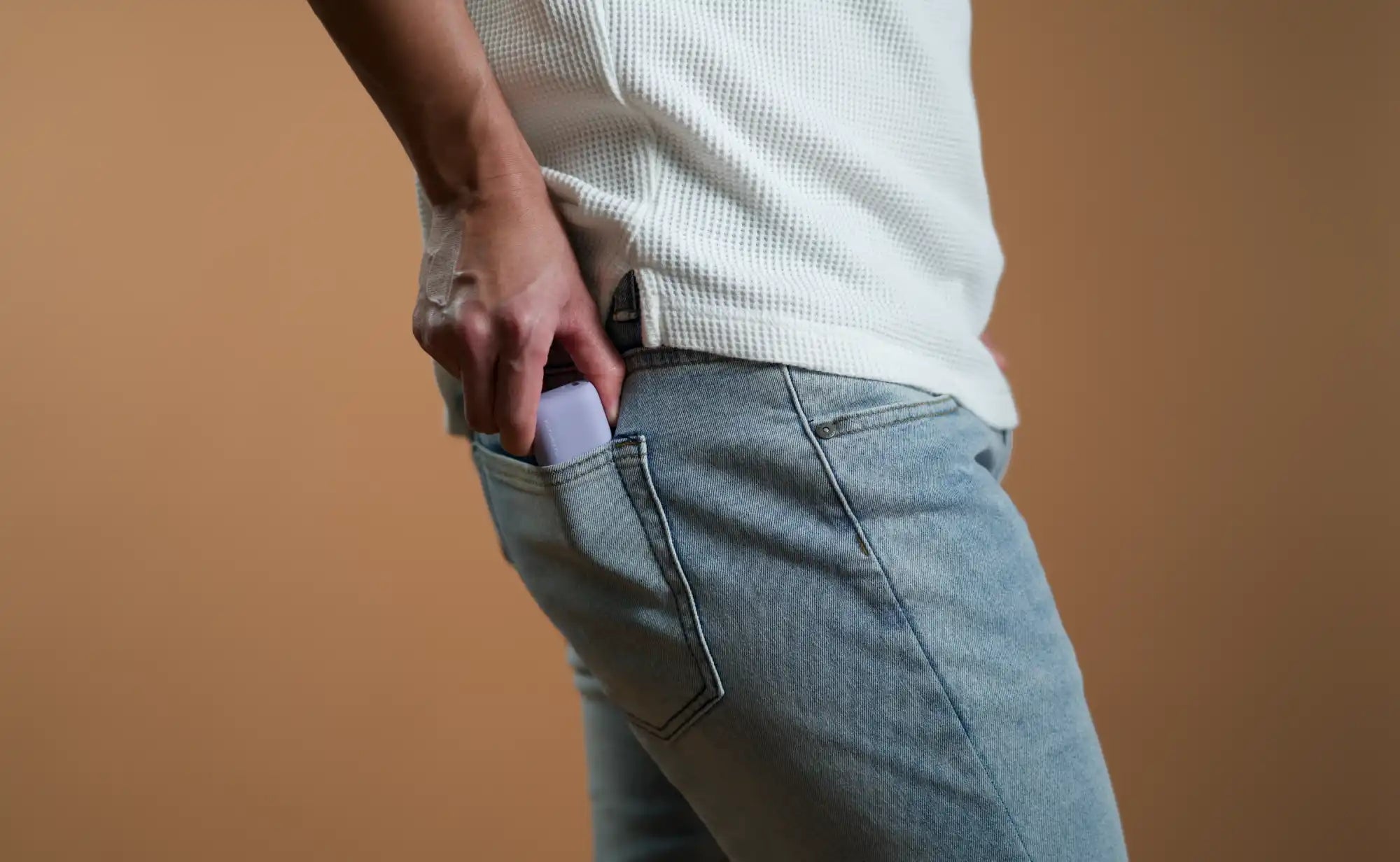 Person putting a purple object in their jeans pocket.