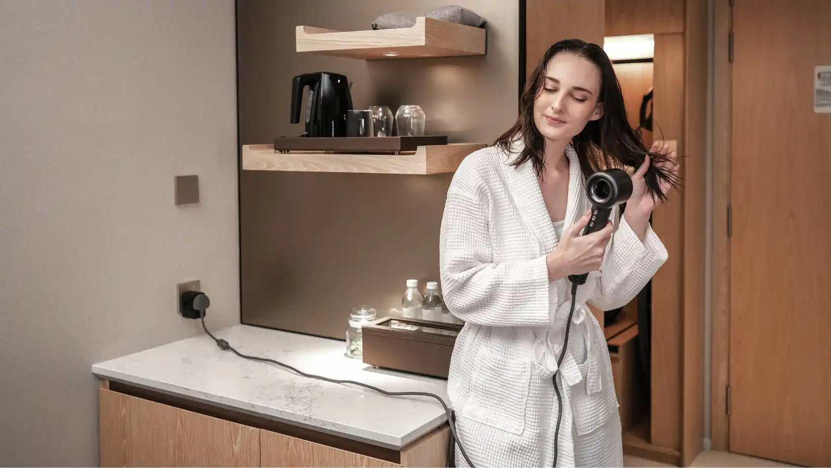 Woman in bathrobe using hair dryer.