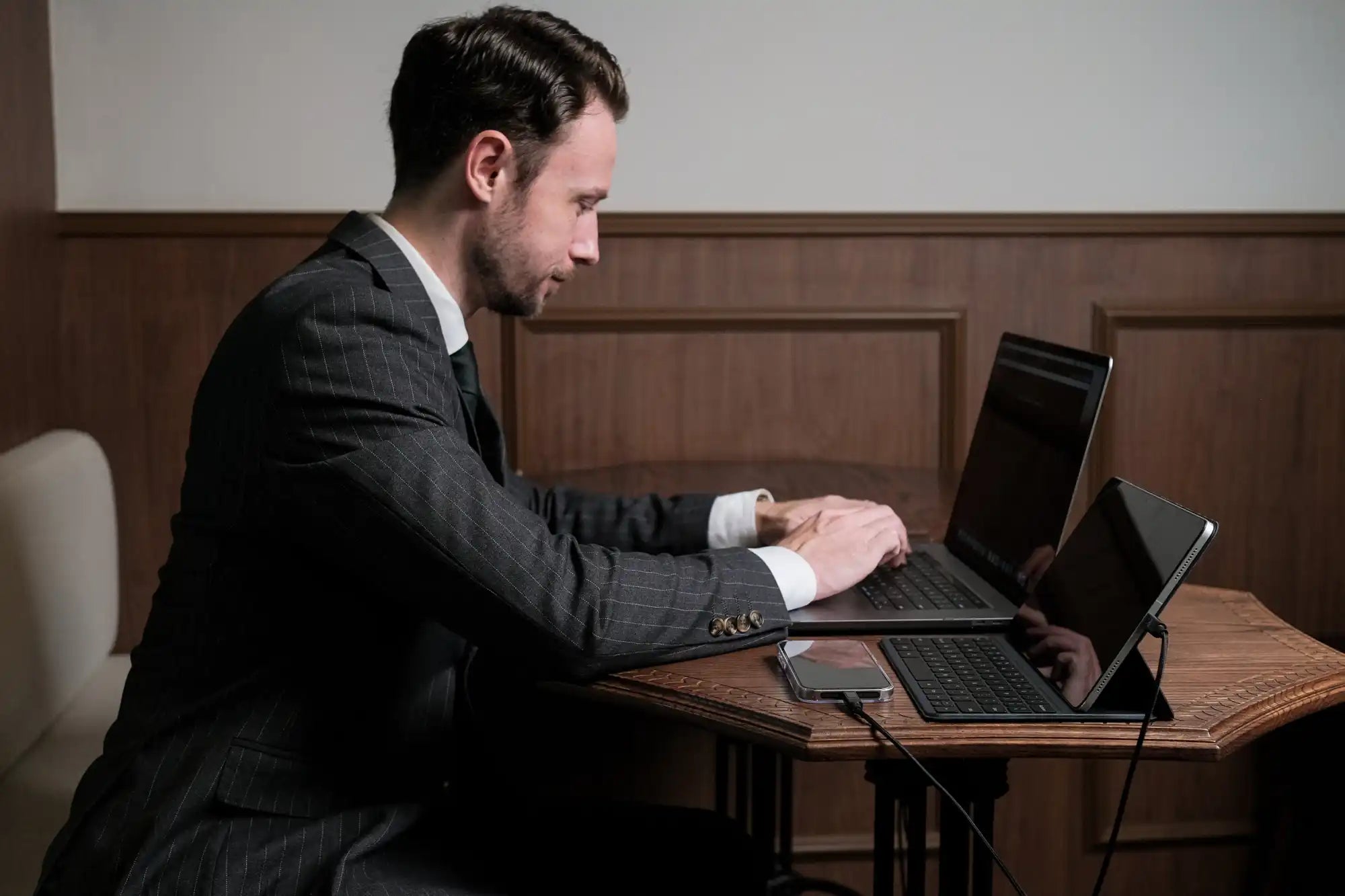 Man in suit using laptop and tablet.